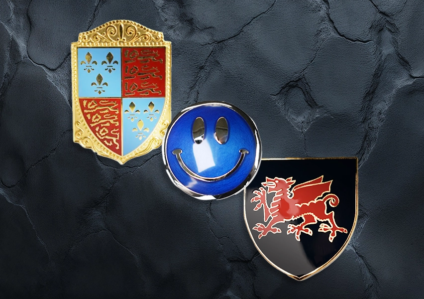 A top-down view of various custom enamel pin badges showcasing their vibrant colors and intricate designs against a dark basalt rock background.
