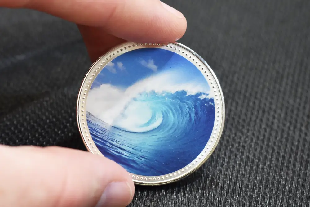 Hand holding a silver collector coin with full-colour ECO UV print, ocean wave design, 38.6mm